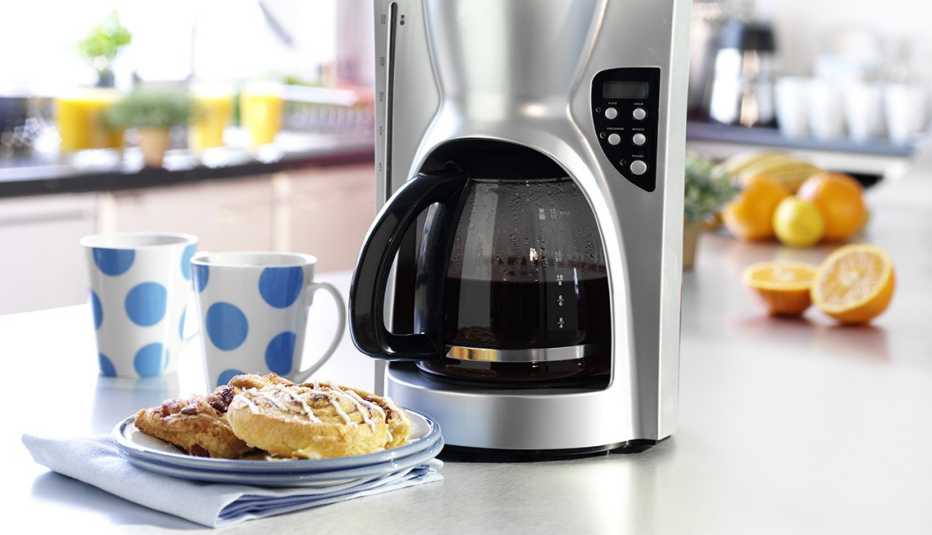 Cafetera eléctrica sobre un mesón con dos galletas y dos tazas