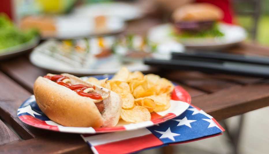 Perro caliente con papas fritas en una barbacoa, junto a otros artículos de picnic en el fondo