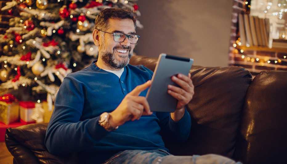 Hombre sentado frente a tableta con un árbol de Navidad de fondo