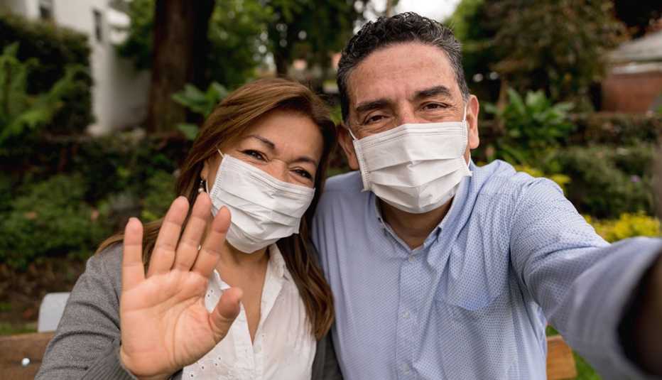 Pareja posando para una foto, mientras llevan puesta una mascarilla quirúrgica al aire libre