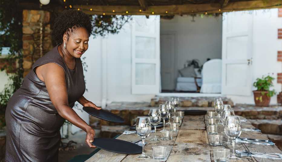 Mujer sonriente que viste un traje de noche y arregla una mesa para una cena 