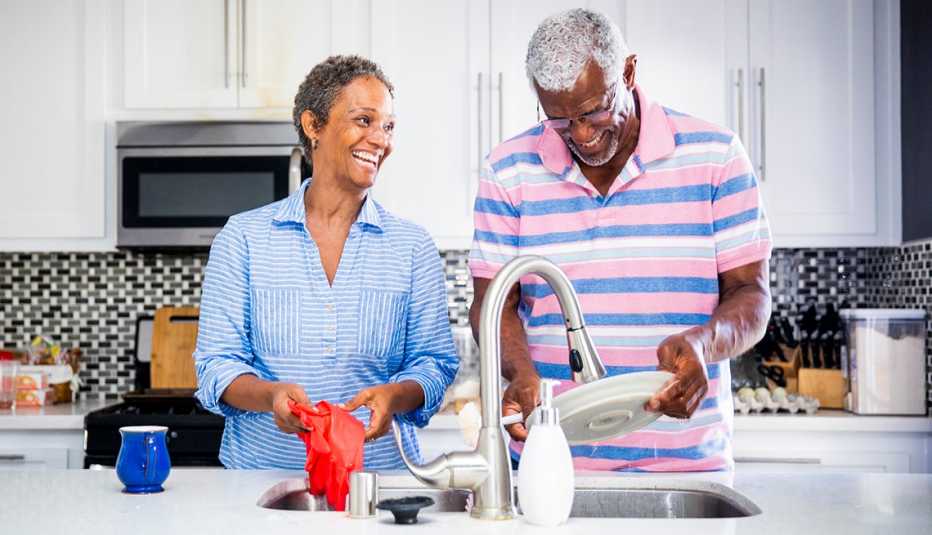 Pareja en la cocina lava los platos mientras y sonríe