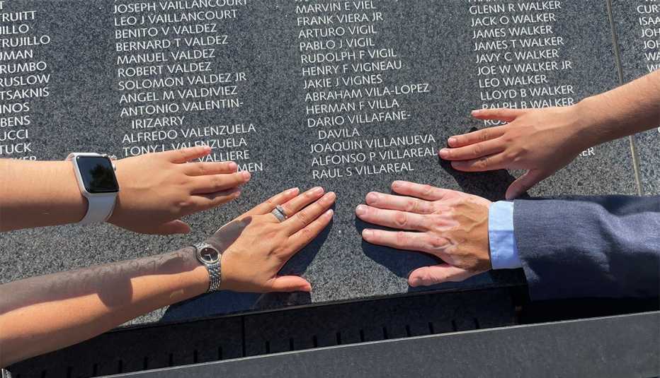 Manos de familiares y amigos tocando el muro conmemorativo