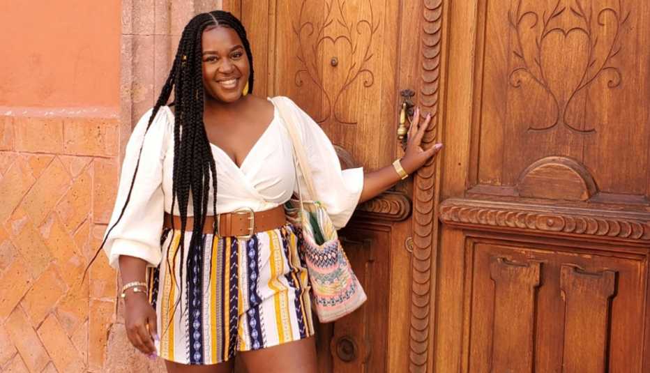 La ganadora de Benefits Badass, de AARP, Jihane Jeanty, de pie frente a una puerta de madera.