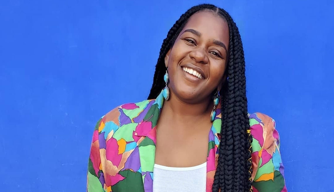 La ganadora de Benefits Badass, de AARP, Jihane Jeanty, de pie frente a un fondo azul.