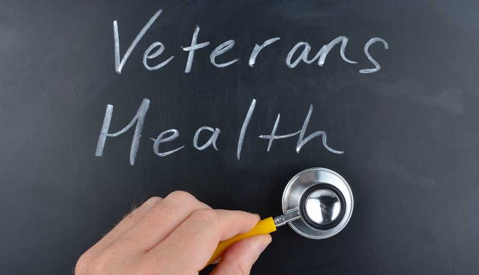 Salud de los veteranos escrita a mano en una pizarra con tiza blanca con la mano de un médico sosteniendo un estetoscopio.