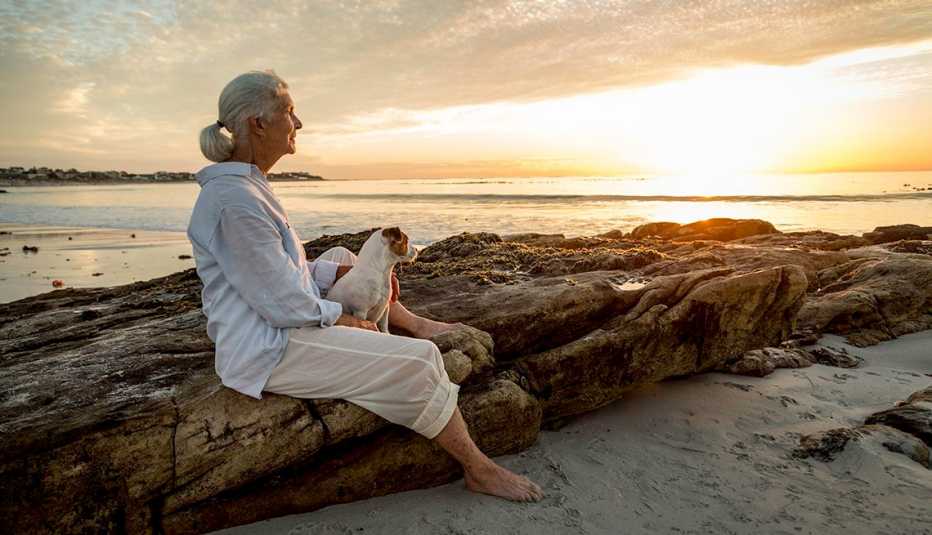 Una mujer con su perro observa el atardecer en una playa