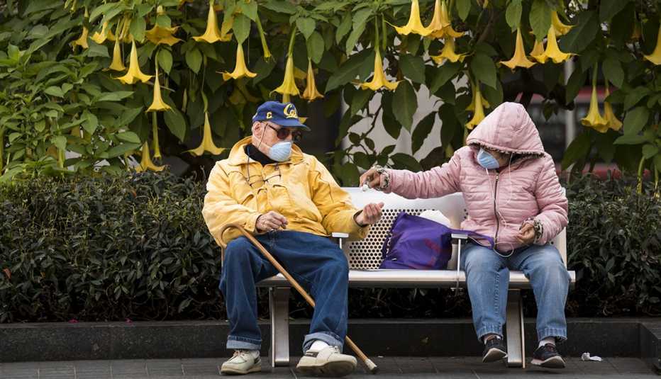 Pareja sentada en un banco usando mascarillas protectoras