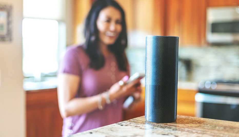 Mujer en la cocina sostiene su teléfono frente a un dispositivo de altavoz inteligente