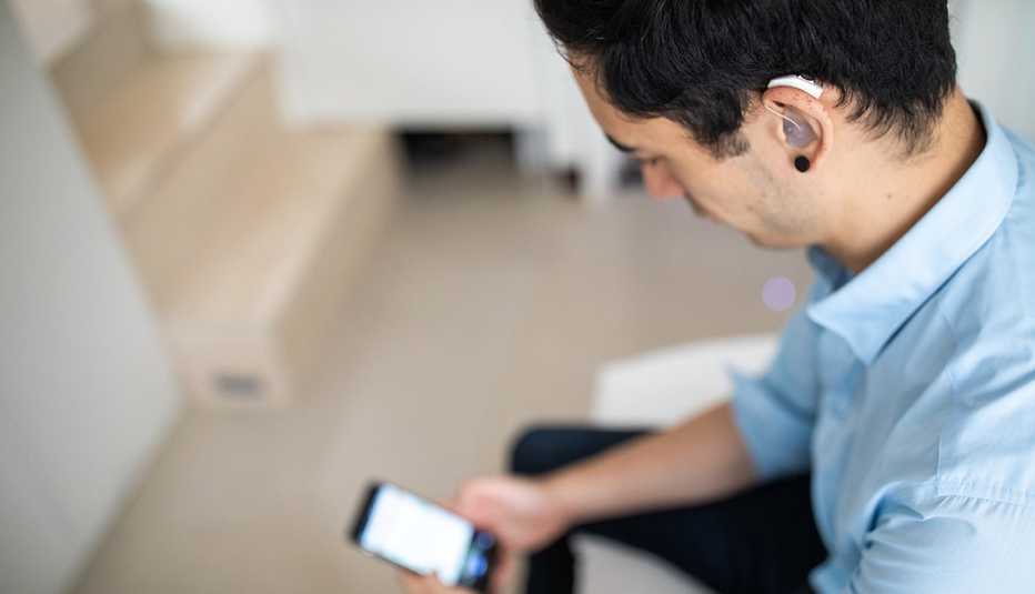 Un hombre con audífono en el oído mira su teléfono
