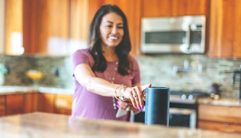 Mujer en su cocina tocando un dispositivo de altavoz inteligente