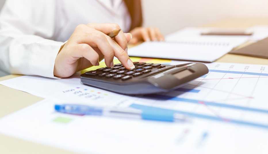 Manos de una mujer sobre una calculadora y papeles en un escritorio.