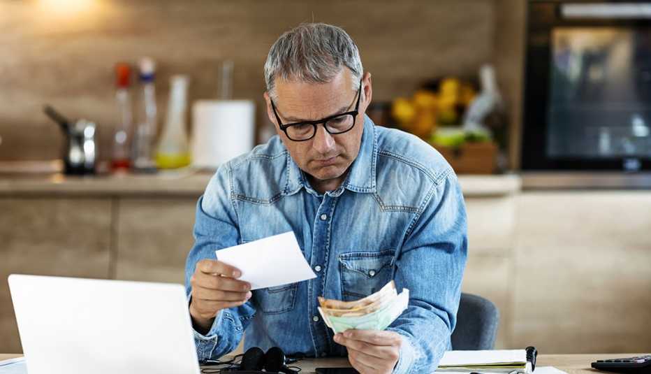 Hombre en la cocina de su casa y revisando cuentas frente a su computadora.