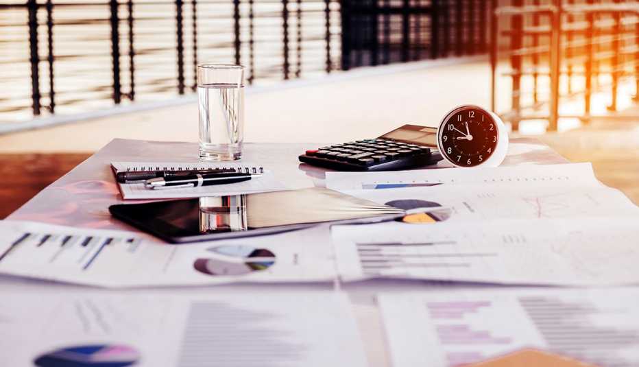 Escritorio con documentos financieros, una tableta, un reloj, un vaso, una calculadora