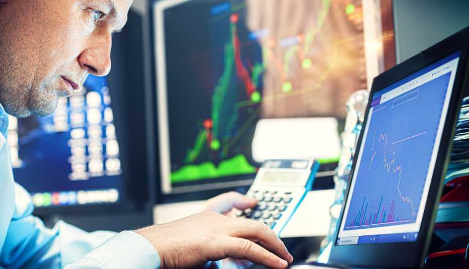 Persona frente a una computadora viendo estadísticas de inversión financiera en tres pantallas.