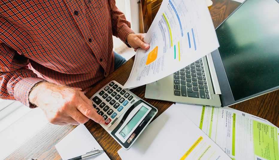 Persona haciendo cuentas sostiene facturas en la mano y hace cuentas en una calculadora