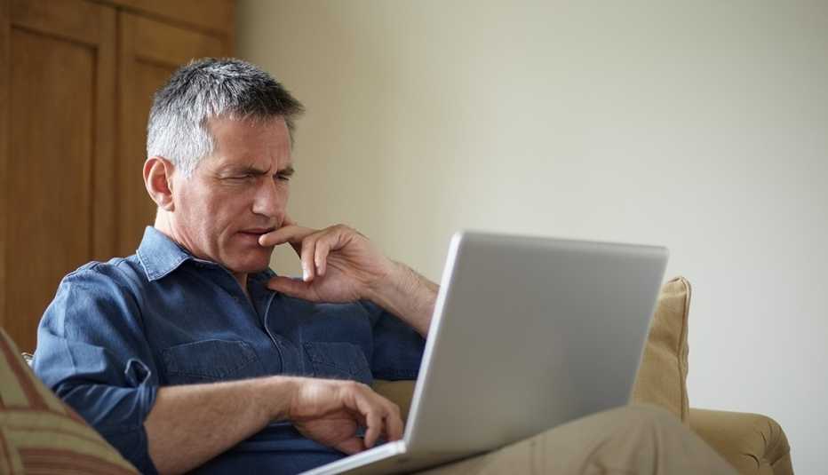 Hombre mirando una computadora personal sobre sus piernas en una sala.