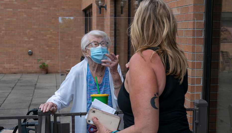 Una mujer mayor habla con otra más joven con una barrera protectora en medio