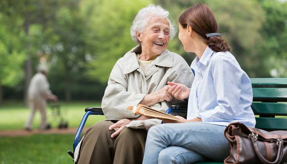 Madre e hija adultas disfrutan de un día al aire libre, sentadas en un banco en un parque.