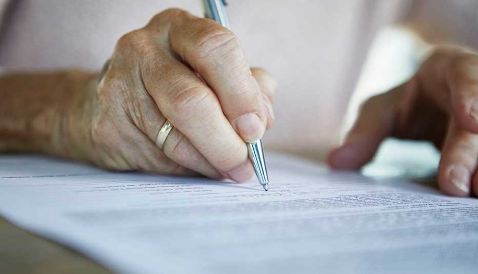 Mano de una persona mayor firmando un documento.