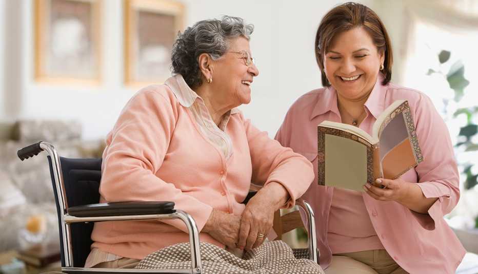 Una mujer leyendo un libro a su madre que está sentada en una silla de ruedas.