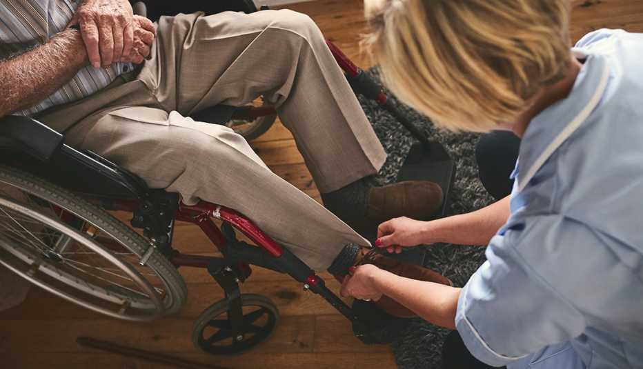 Mujer amarra los zapatos de un hombre en silla de ruedas