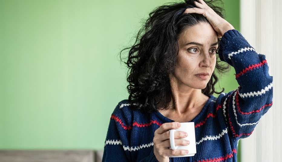 Una mujer con una taza en la mano y luce preocupada
