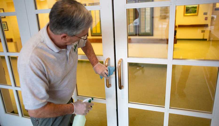 Un hombre, usando protección, limpia y desifencta una puerta