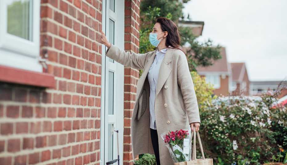 Una mujer, usando mascarilla, toca una puerta de una casa