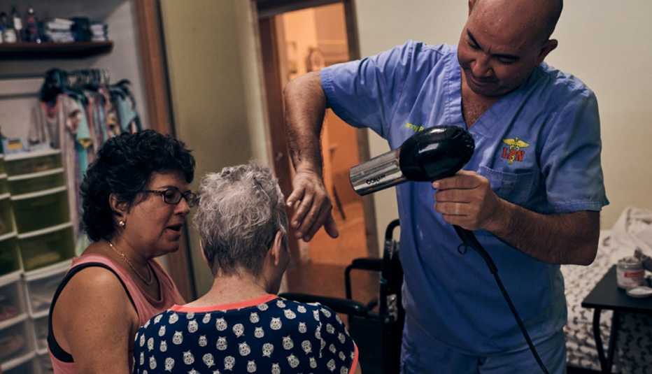 Asistente le seca el pelo a una mujer mayor mientras su hija observa