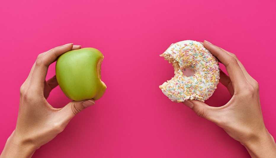 Dos manos, una sostiene una manzana y la otra una dona