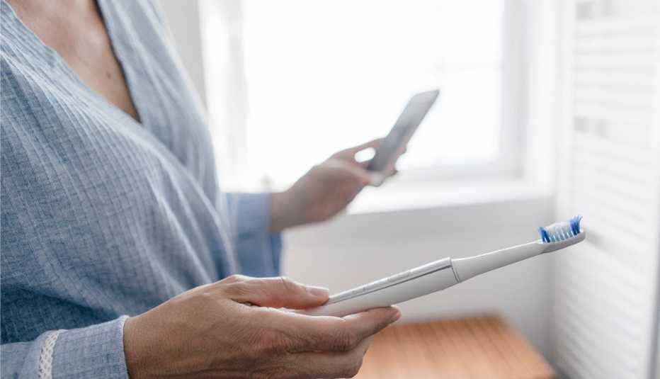 Una mujer sostiene un cepillo de dientes y su teléfono celular