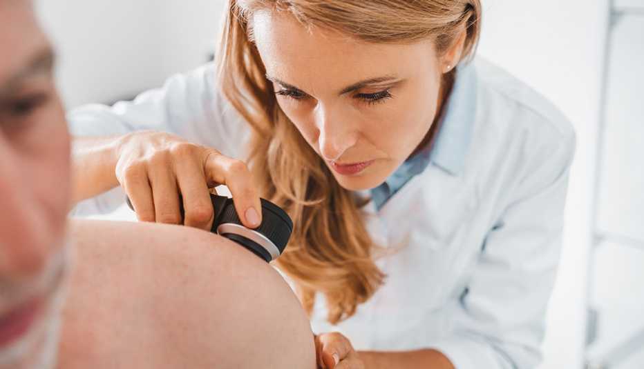 Una dermatóloga examina la piel de la espalda de un paciente.