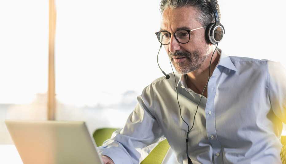 Un hombre con audífonos frente a una computadora atiende una videoconferencia