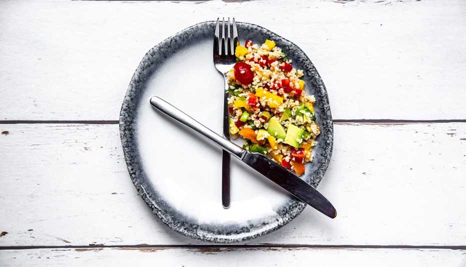 Ensalada en un lado de un plato y los cubiertos simulando un reloj