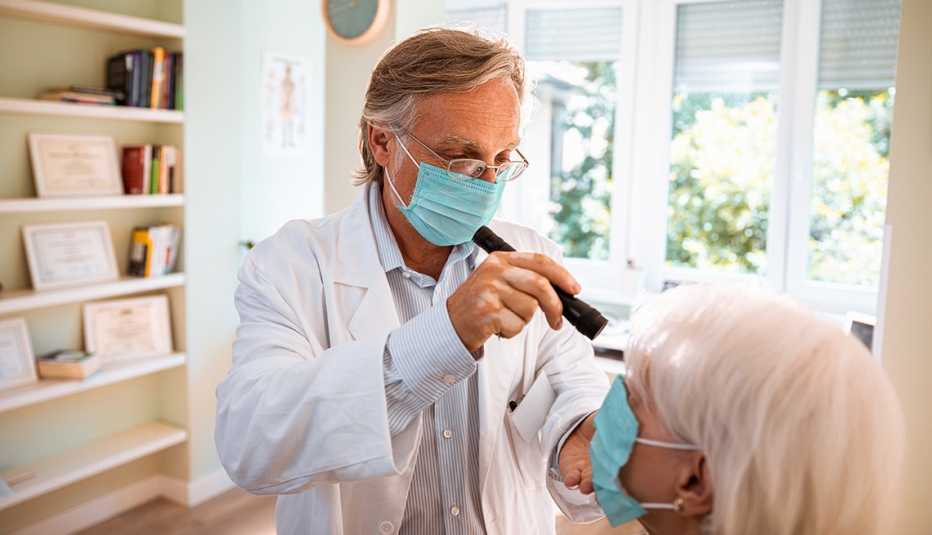 Médico examina los ojos de su paciente, ambos usan mascarillas