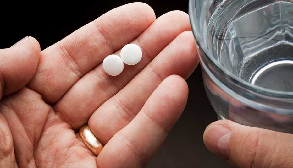 Un hombre sostiene unas pastillas en una mano y un vaso de agua en la otra