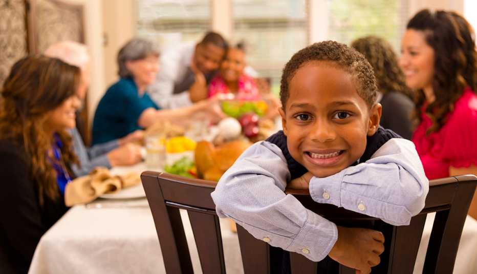 Niño sonríe mientras la familia está atrás suyo cenando