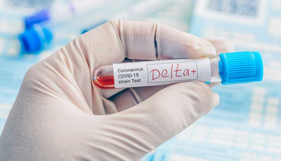 Una mano con guantes sostiene un tubo de ensayo que dice Delta+