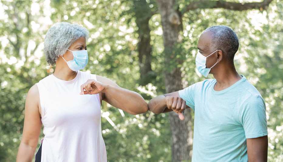 Un hombre y una mujer, ambos usando mascarilla, se saludan con el codo