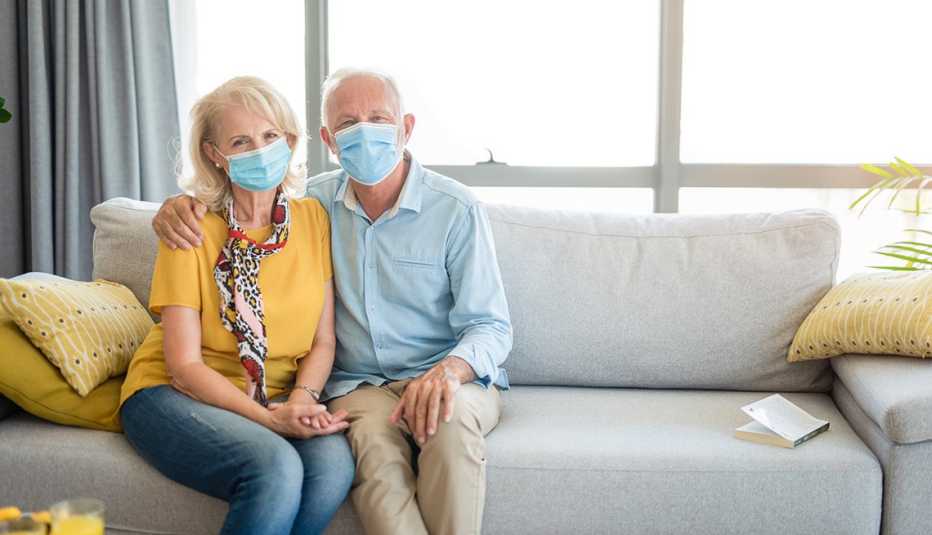 Una pareja mayor sentados en un sofá y usando mascarillas