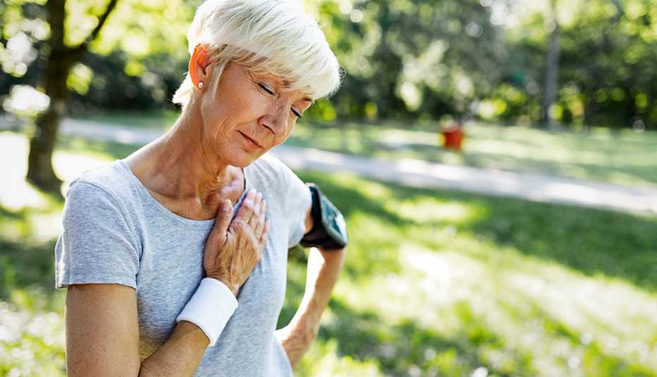 Una mujer, que se ejercita al aire libre, se detiene y se toca el pecho en señal de dolor.