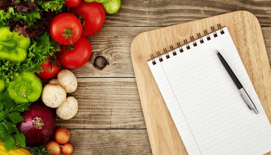 Una libreta de notas, un bolígrafo y vegetales sobre una mesa