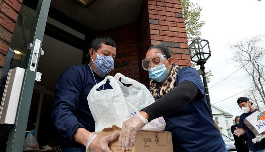 Una mujer le entrega una caja con alimentos a una mujer, ambos usan mascarillas