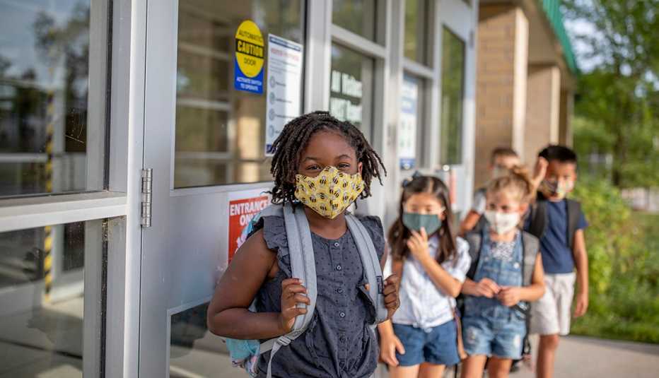 Grupo de niños en fila, cada uno con su mascarilla y listos para entrar a un salón de clases