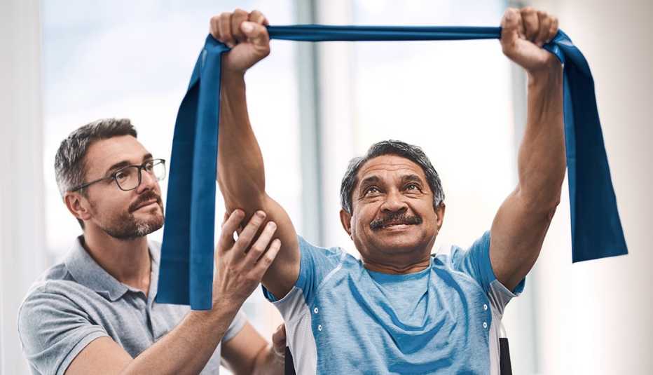 Un hombre usa bandas elásticas para estirar sus brazos con la ayuda de un entrenador personal