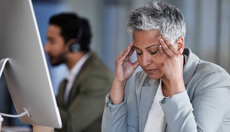 Una mujer, en una oficina, con sus ojos cerrados y manos en la sien
