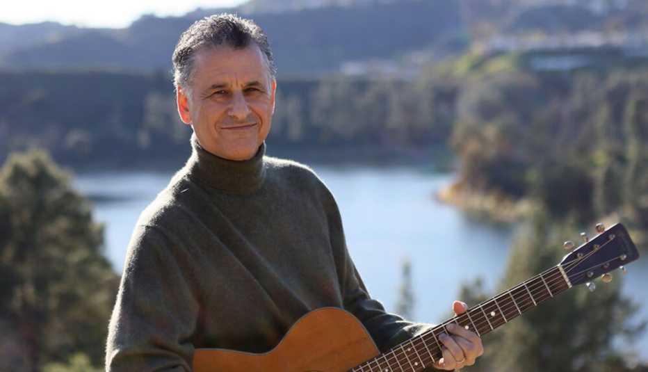 Daniel Levitin con guitarra en mano y de fondo un lago rodeado de árboles