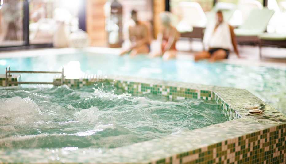 Vista de un jacuzzi y al fondo tres personas sentadas al borde de una piscina