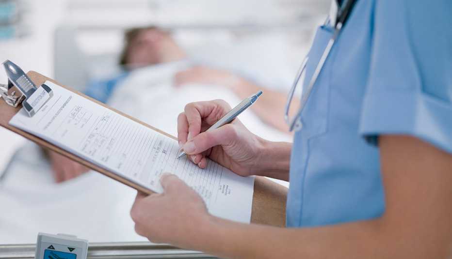 Un doctor llena un formulario de un paciente que se ve acostado al fondo.